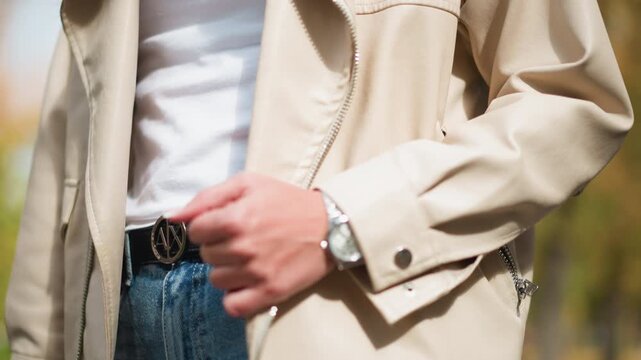 Close up of woman wearing beige jacket white shirt and blue jeans with her hand adjusting zipper. watch on her wrist is visible along with details like stitching patterns in fabric. Soft