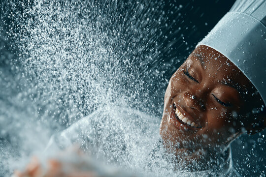 Happy chef wearing white hat experiencing water splash in kitchen with restaurant worker