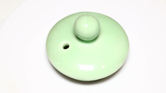 A white bowl with a green lid sitting on a table, perfect for a rustic or vintage-themed setting. Rotating in a circle