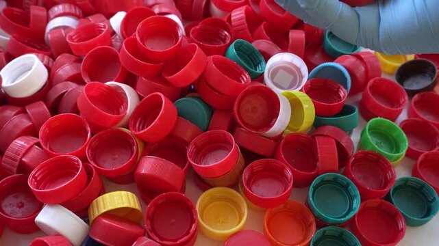 A gloved hand holds the red caps in close-up. A detail of the plastic sorting process.