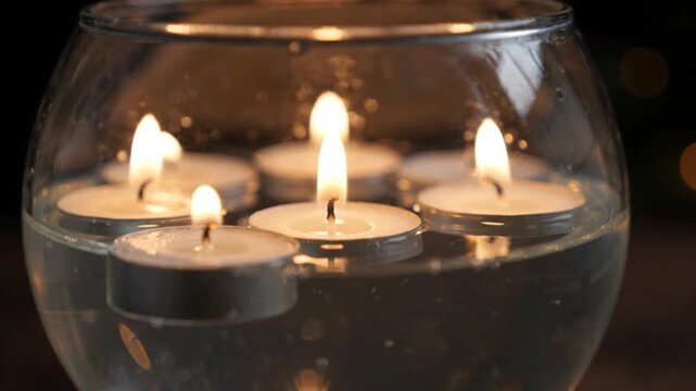 Floating tea light candles glowing inside a glass bowl filled with water