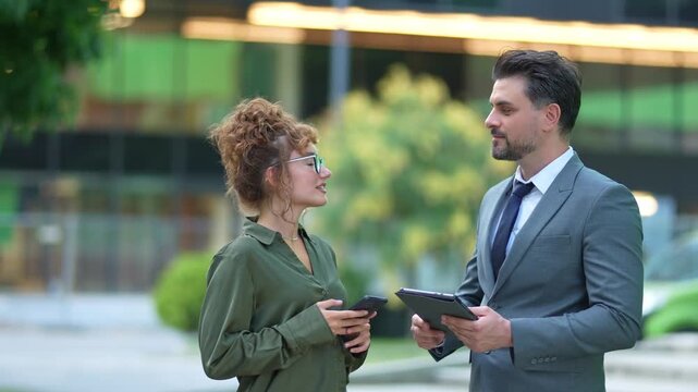 Two business people talking and using devices outdoors