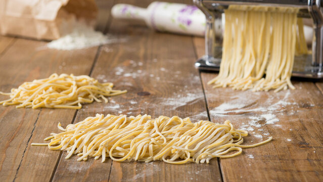 Freshly Made Pasta Dough Being Cut by a Machine on a Wooden Surface