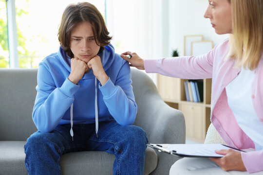 Psychologist comforting teenage boy during consultation in office, closeup