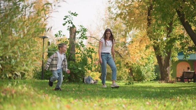 Family playing soccer in park with green grass and autumn trees. woman man and young boy interact near black and white soccer ball under bright daylight. bench is visible on right side