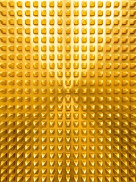 Full frame close up view of golden brass metal surface featuring 3D studded pyramid spike grid pattern for luxury background and abstract texture design