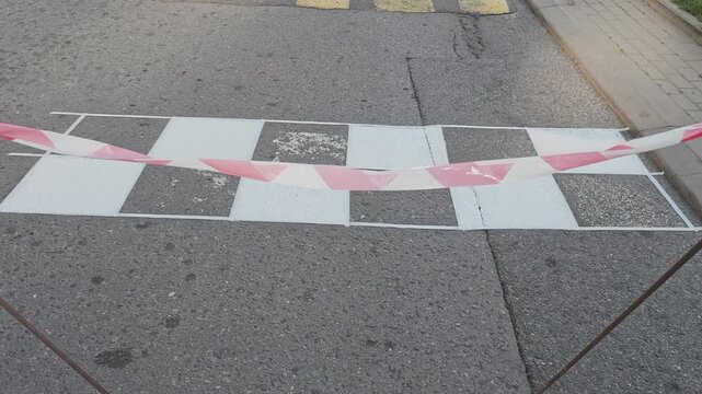 Newly painted black and white checkered finish line on an asphalt road. A red and white warning tape protects the wet paint while it's drying