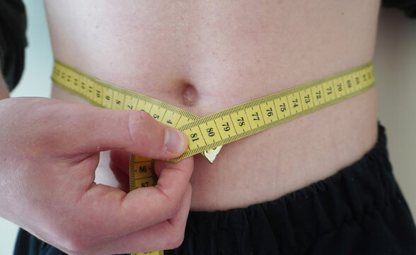  Person measuring waist with yellow tape measure. Hands holding the tape around the belly. Weight control concept.