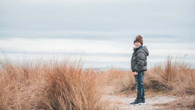 Smiling boy in a beanie stands among coastal dune grass