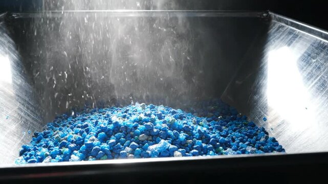 Industrial hopper dispensing blue plastic pellets in a manufacturing factory
