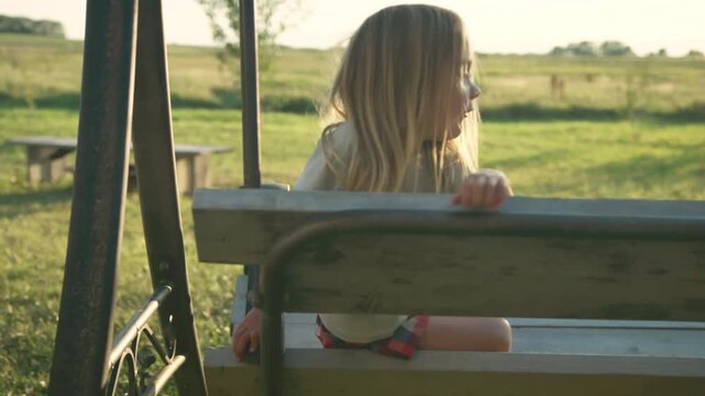 Boy climbing and playing on old wooden swing set in rural field at golden hour