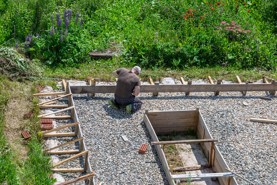 Man builder working on wooden formwork for strip foundation construction. Laying concrete footing shuttering on gravel bed for house garage base. Diy construction site in backyard