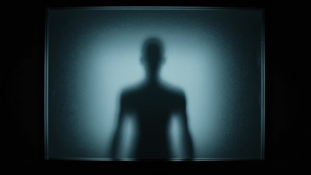 Scary human silhouette slowly appearing behind frosted glass in darkness, eerie halloween horror shadow figure creating fear, mystery and supernatural nightmare motion video