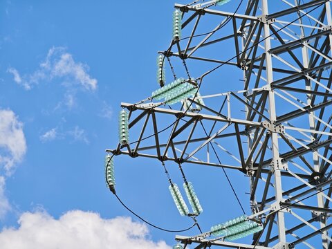 High voltage electrical transmission tower with glass insulators against a blue sky, conveying energy distribution and power grid infrastructure.