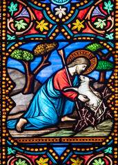 Obraz premium Jesus Christ rescues a trapped lamb from thorny bushes in a colorful stained glass window detail.