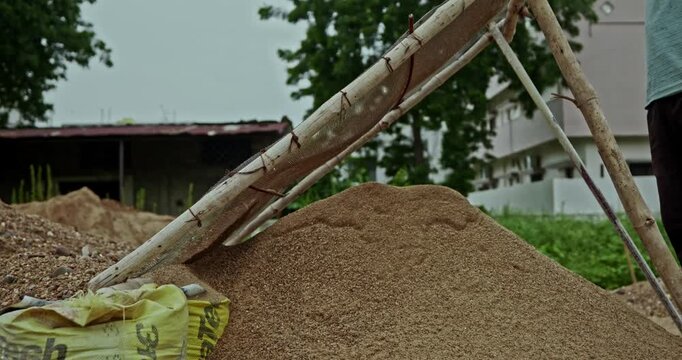 Construction Laborers Preparing Sand at an Indian Building Site Using a Handheld Metal Sieve. Skilled manual workers perform traditional sand screening work during ongoing construction activities