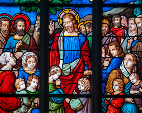A stained glass window depicts Jesus Christ surrounding himself with children.