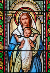Obraz premium A stained glass window depicts the Virgin Mary holding the infant Jesus in detailed artwork.