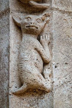 A stone relief sculpture depicts a grotesque creature carved into an ancient medieval portal pillar.
