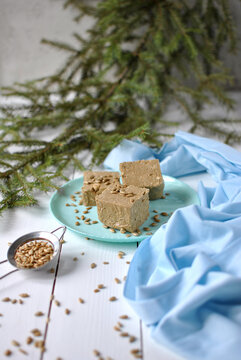 Sunflower halva cubes topped with seeds on a turquoise plate, styled with blue fabric and evergreen branches.