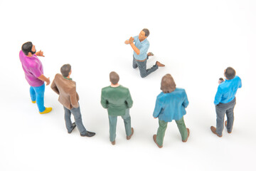 Obraz premium Miniature people in a meeting with one kneeling and speaking to a group on a plain background