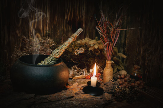 Mystical autumn witchy altar with steaming iron cauldron, dried herbs, burning candle and magic tools.