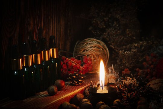 Authentic altar of the village witch. Glass jars with potion, burning candle, dried herbs, a ball of natural twine and red berries on wooden background, close-up.