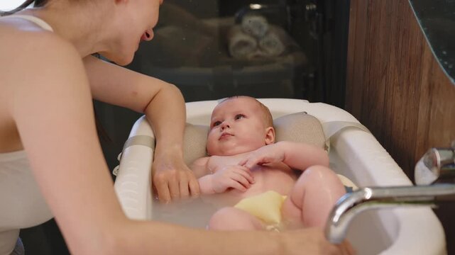 Close-up of a parent arm gently washing a baby during bath time in a baby tub. The baby bath washing in tub shows child infant parent arm water hygiene clean care