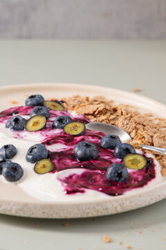 Healthy breakfast bowl with yogurt, fresh blueberries, berry jam swirl, and crispy whole wheat flakes on a textured ceramic plate