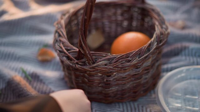 Close up of wicker basket containing orange on soft fabric with scattered food items. scene includes natural light and subtle shadows focusing on texture details of woven material