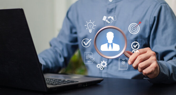 Talent acquisition, human resources, hiring, recruitment, and evaluation. Professional recruiter reviewing a candidate profile with a magnifying glass beside a laptop.