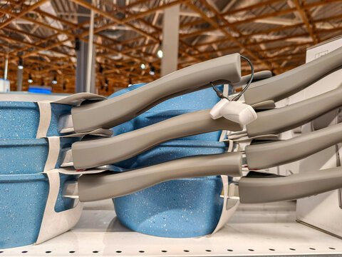 Blue frying pan with anti theft security tag on handle displayed on retail shelf. Kitchenware cookware stock in supermarket. Cooking supply equipment and home goods shopping concept