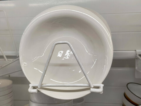 White ceramic plate on a metal display stand in a retail store. Kitchenware department shelf with tableware products. Minimalist home decor item for dining and dinner table setting