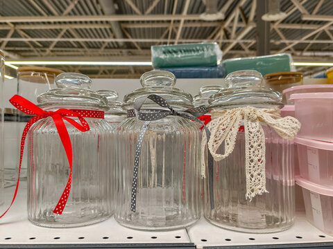 Glass jars with lids and ribbons on a retail store shelf. Decorative kitchen storage containers for home organization. Tableware displayed in a supermarket for interior design