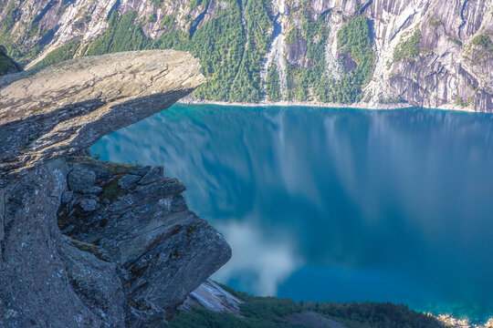 View from the cliff edge overlooking a clear blue lake in Norway with steep rocky mountains around