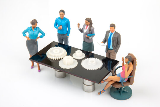 Miniature figures in a business meeting around a table with gears and tools