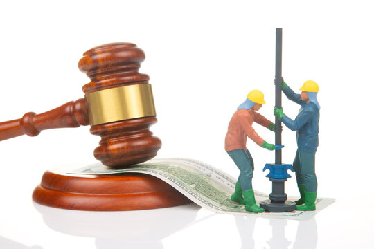 Miniature figures doing construction work near a gavel and dollar bills on a white background