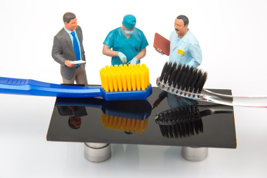 Miniature people discussing dental tools with toothbrushes on a black surface