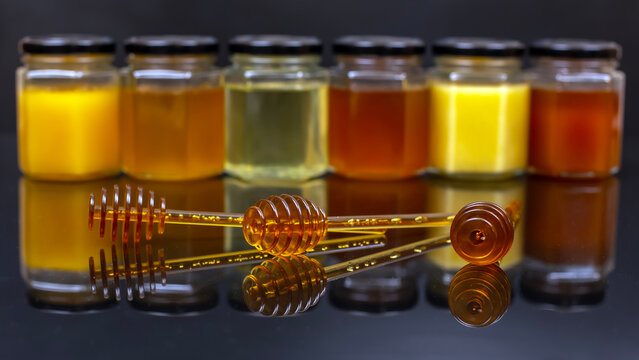 Different types of honey displayed in jars with honey dippers on a reflective surface