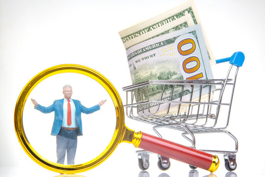 Miniature figures in a shopping cart with cash and a magnifying glass in a creative setting