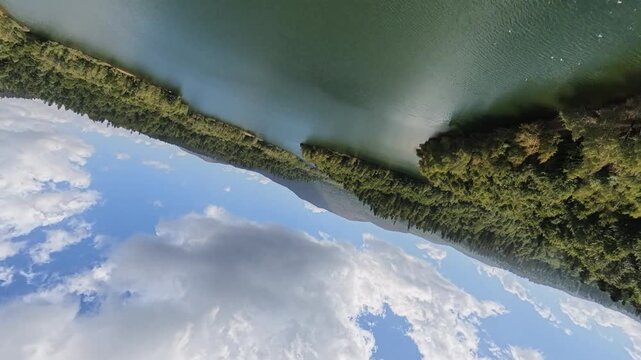 Aerial drone footage showcasing a scenic forest and mountain landscape with a large lake occupying much of the frame. The camera performs a continuous 360-degree rotation, revealing the lake, dense wo