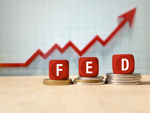 Wooden FED blocks on coins with an upward financial chart representing monetary policy, interest rates, economic growth, and financial markets.