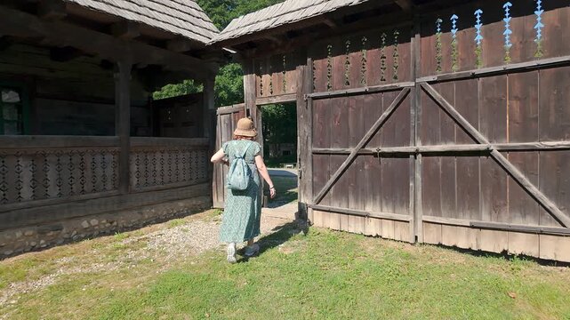 Woman tourist walking beside a large traditional wooden gate and rustic farmhouse in Romania