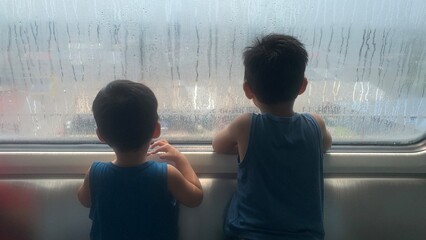 Two children looking through a condensation-covered train window during a urban rail transportation in Kuala Lumpur © MR HEPPY