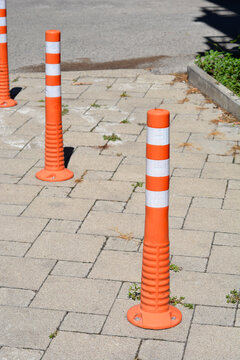 Diagonal view of three orange and white flexible traffic bollards bolted onto a concrete paving slab walkway.