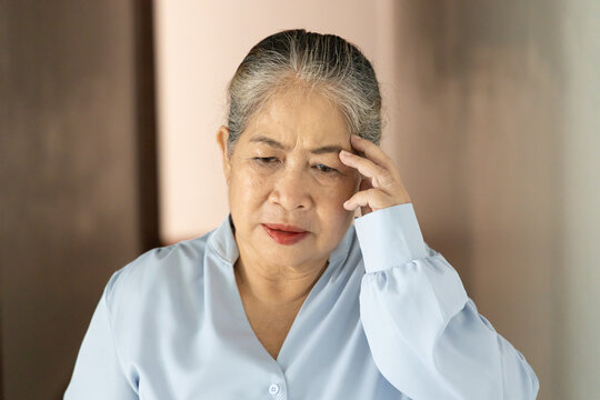 sick asian senior old woman suffering from headache on one side of her head, holding temple in pain