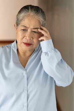 sick asian senior old woman suffering from headache on one side of her head, holding temple in pain