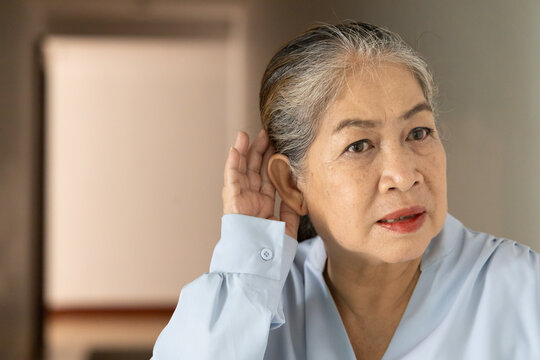 asian senior, late adult woman listening with worried expression and bad feeling, concept image for hard of hearing, hearing problem, indoor scene