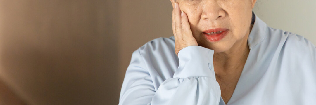 Asian senior, old aged woman suffering from toothache and tooth decay indoors, holding her cheek in pain, dental care concept, body parts closeup shot