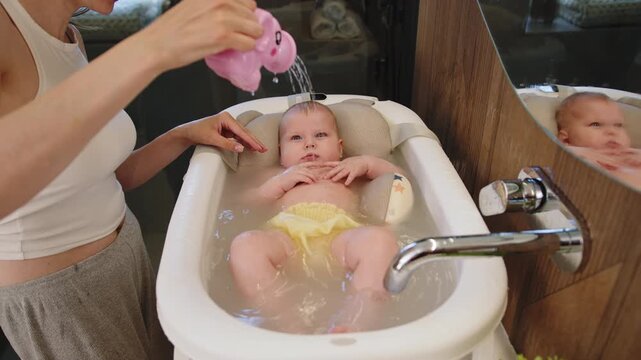 Mother washes baby in bathtub with elephant toy creating joyful moments during bath time routine. A mother bathes baby with care hygiene and joy creating family love and happiness